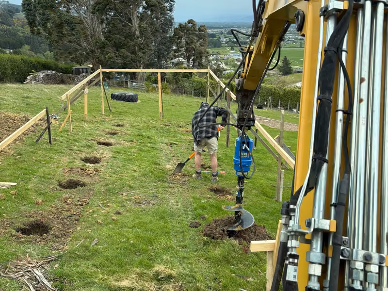 Excavator-mounted auger drilling post holes on rural land