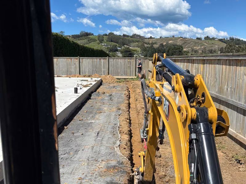 Compact excavator trenching alongside concrete foundations