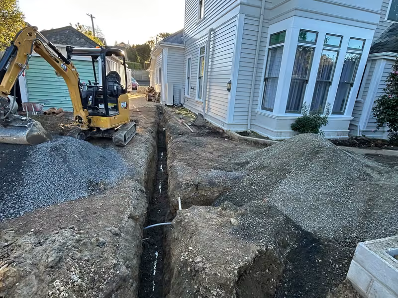 Compact excavator trenching beside a house