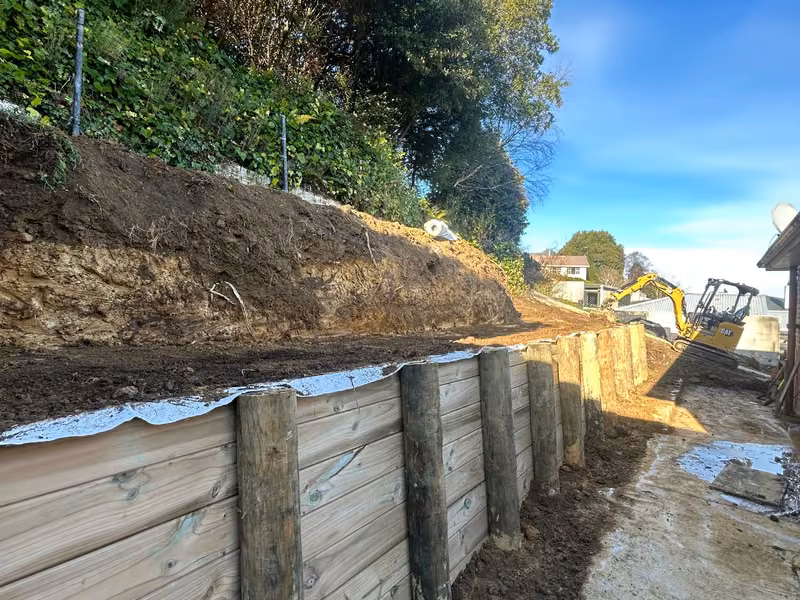 Compact excavator working behind a residential retaining wall