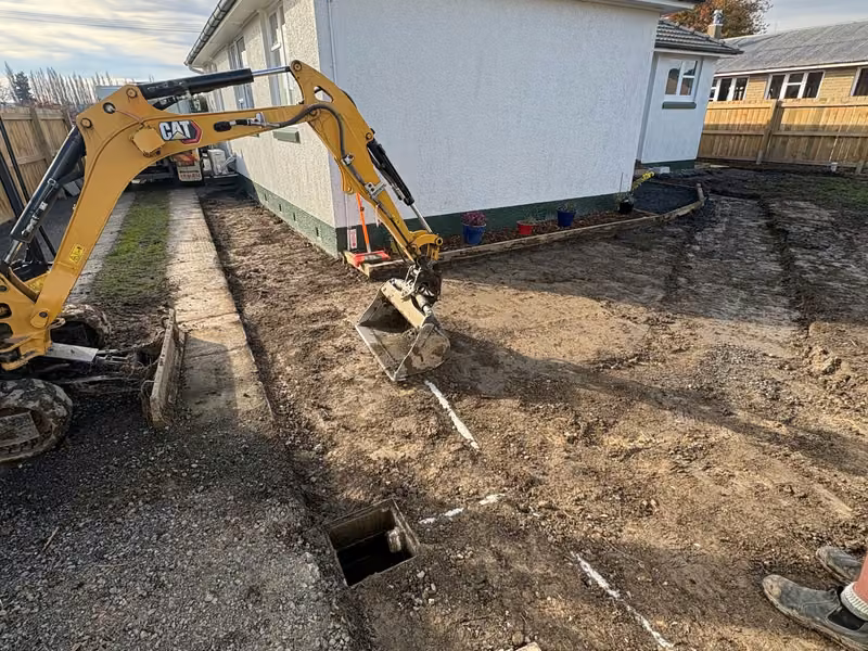 Excavator trenching beside a residential building