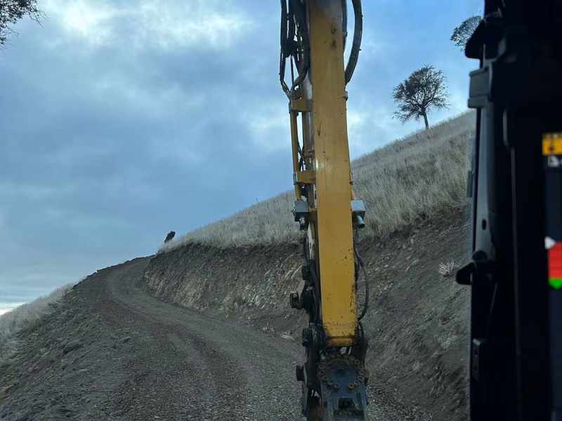 Excavator tracking along a steep formed earthworks cut