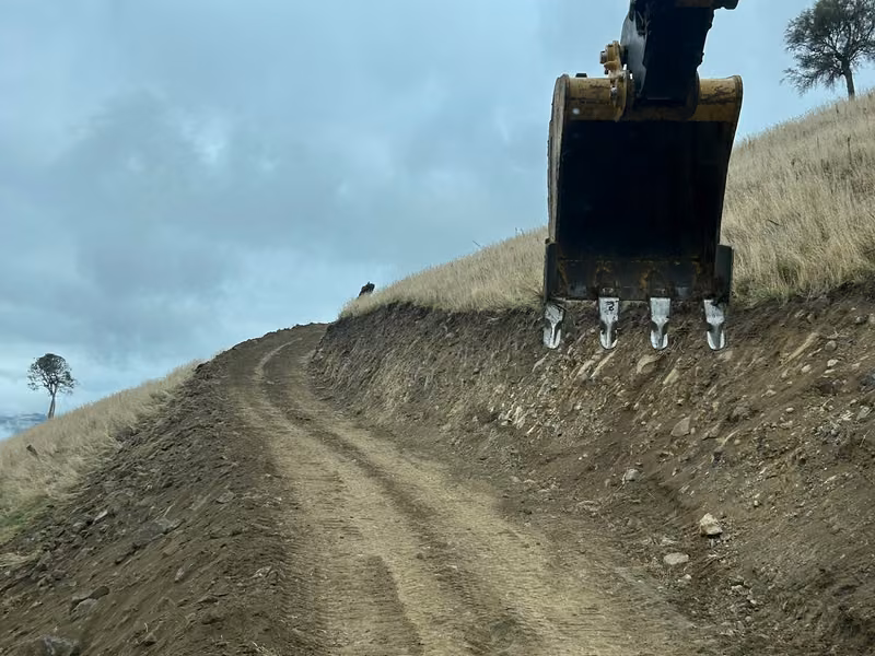 Excavator cutting and shaping an access track on steep terrain