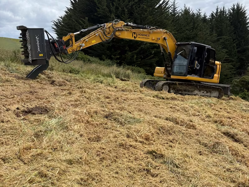 Excavator working across a steep grassed slope